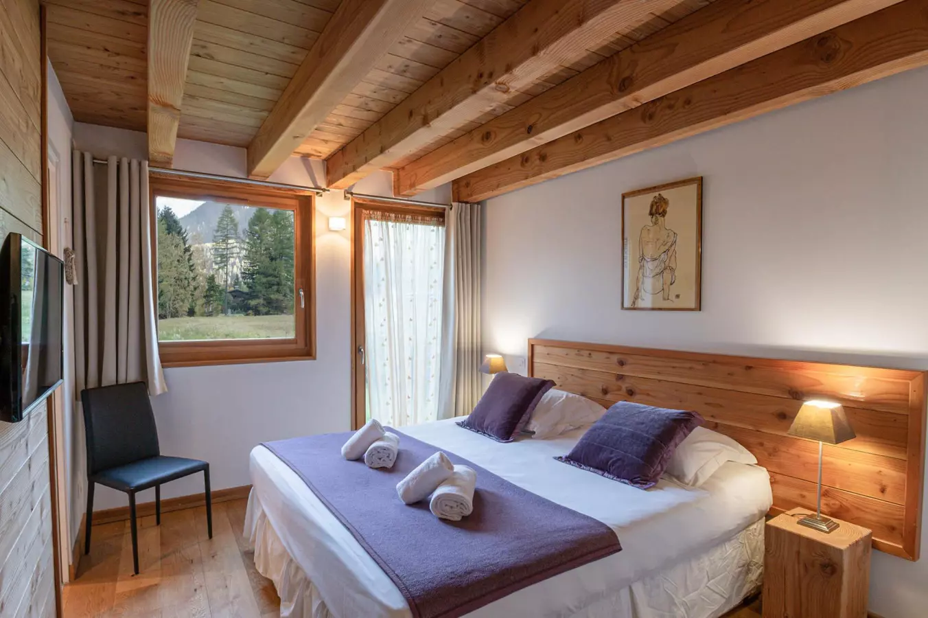Chambre chaleureuse avec lit double, poutres apparentes en bois, et vue sur la montagne depuis les fenêtres.