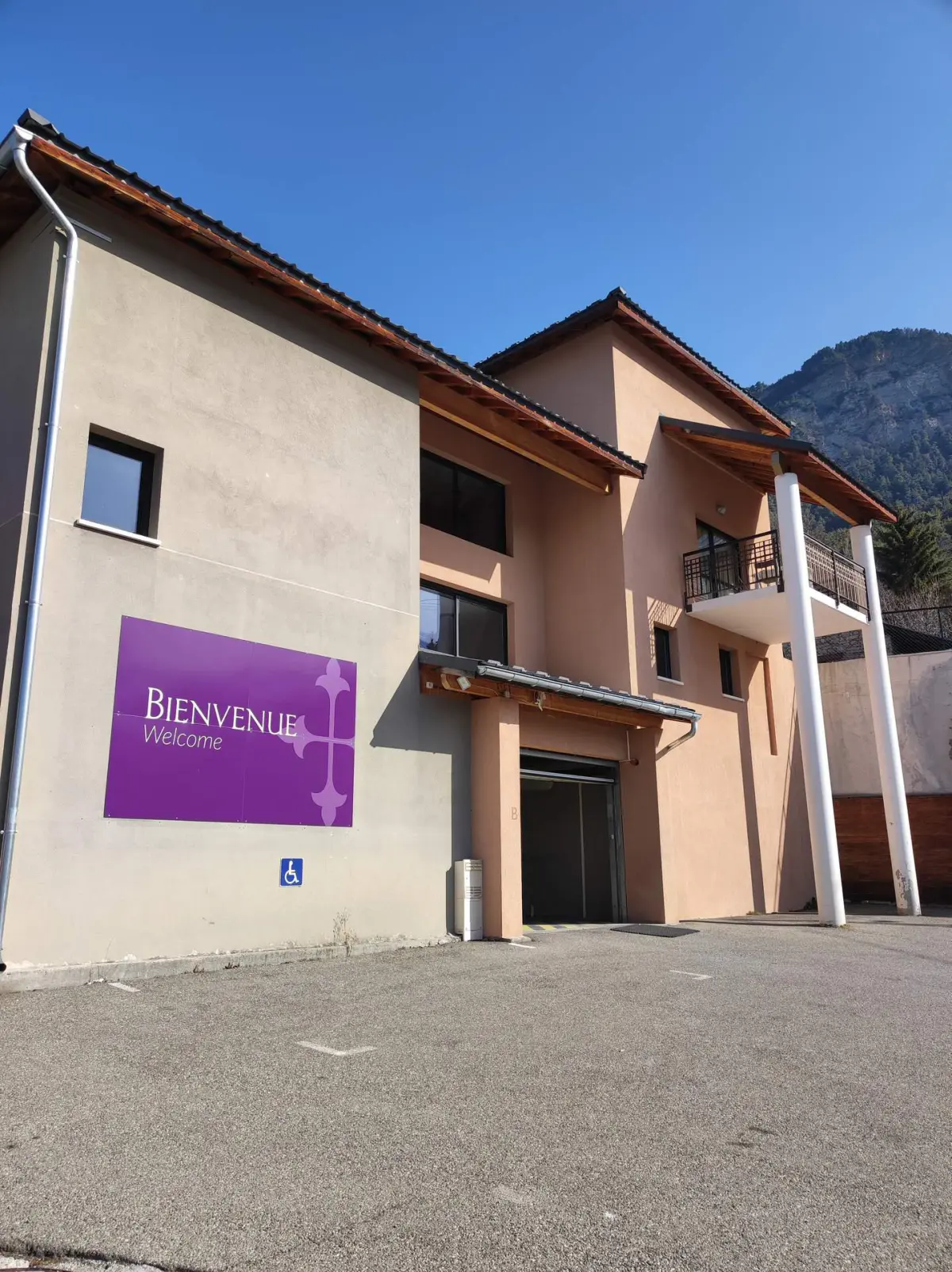 Façade d'un bâtiment moderne avec un panneau violet indiquant "Bienvenue Welcome" sous un ciel bleu clair.