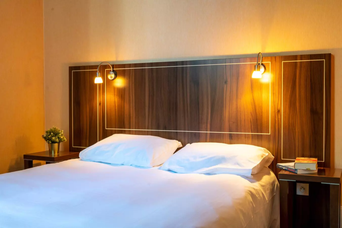 Chambre moderne avec un lit double, tête de lit en bois foncé et deux lampes murales allumées de chaque côté