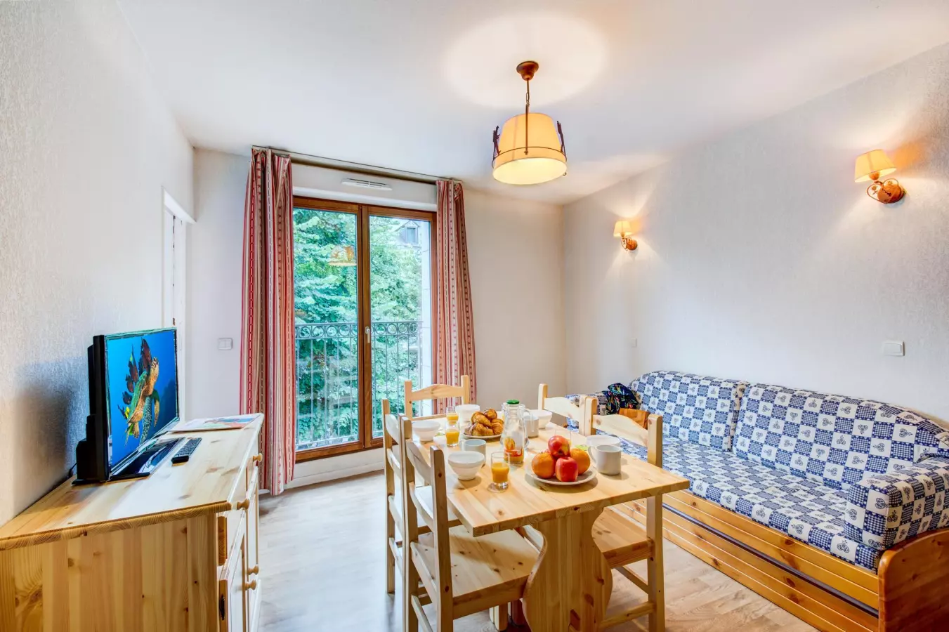 Séjour lumineux d’un appartement de la résidence Illixon, avec mobilier en bois, canapé bleu, coin repas et balcon donnant sur la verdure.