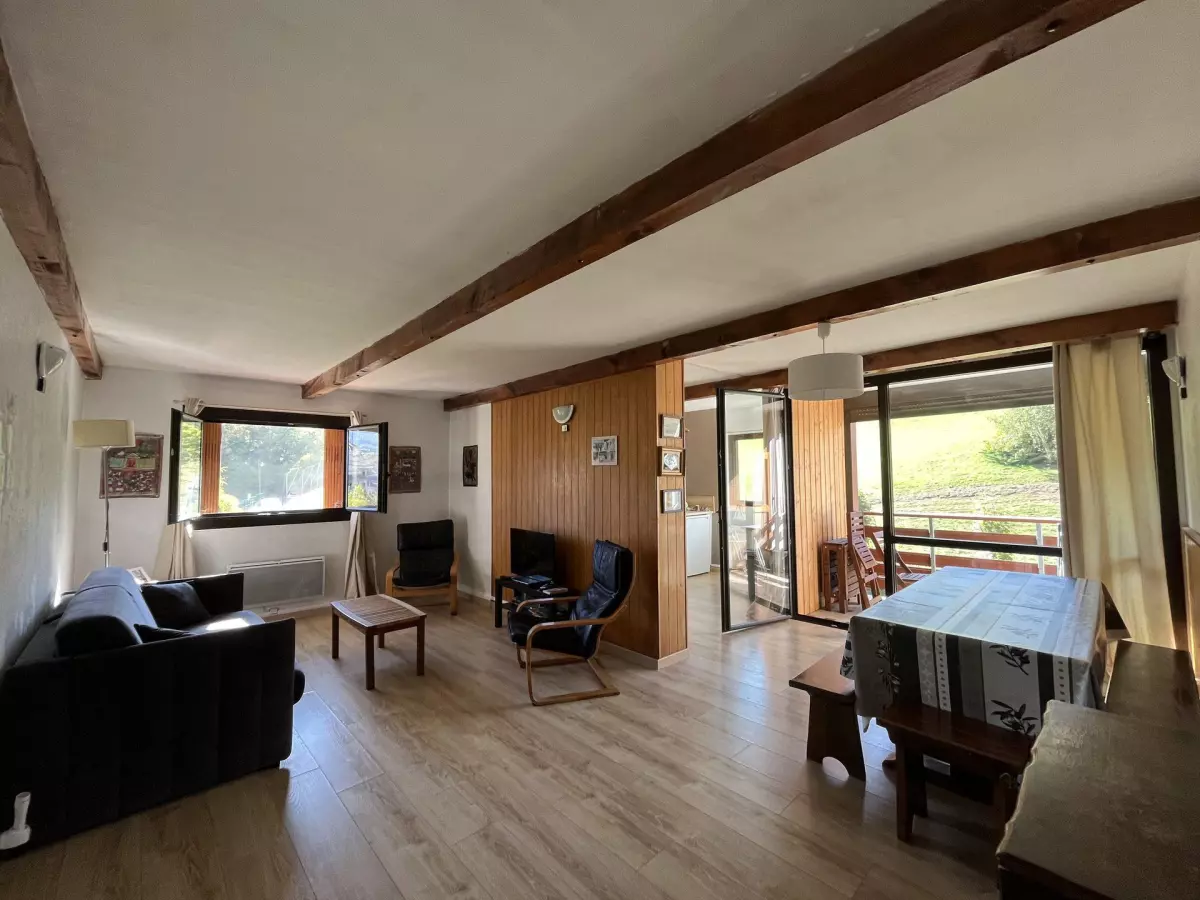 Spacieux séjour lumineux avec poutres apparentes, coin salon, espace repas et accès à un balcon avec vue sur la nature environnante.