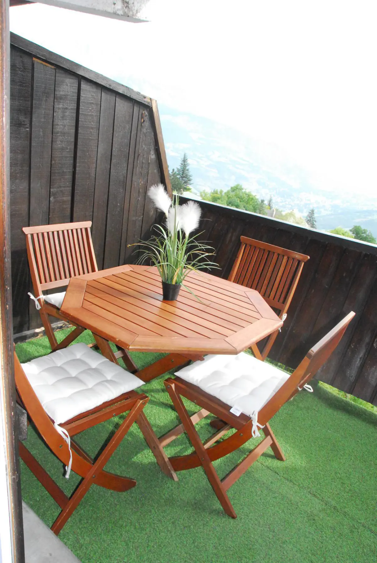 Petit balcon cosy avec table en bois et chaises, gazon synthétique et vue dégagée sur les montagnes, parfait pour un repas en plein air.