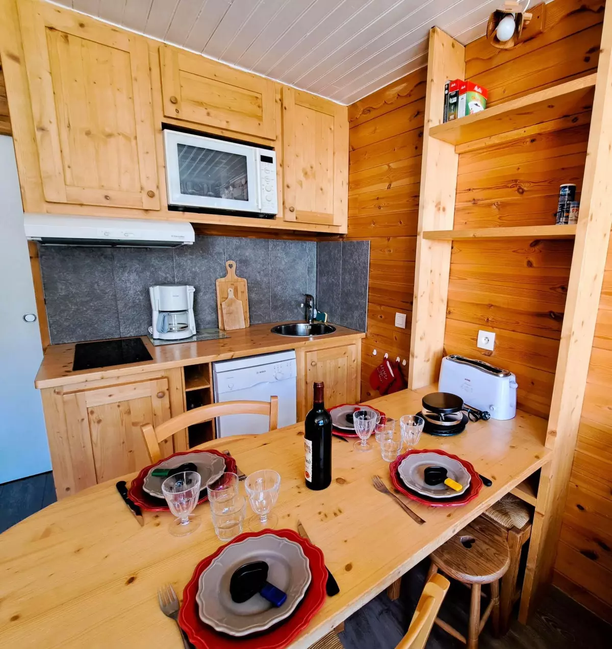 Coin cuisine en bois chaleureux et entièrement équipé avec espace repas convivial, idéal pour les séjours à la montagne.