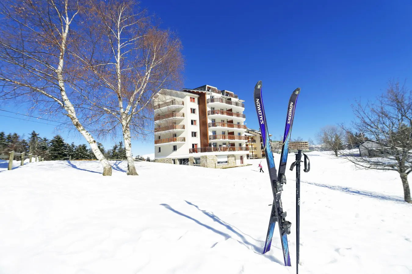 Bâtiment de la résidence Les Balcons d’Ax au cœur d’un paysage enneigé, avec des skis plantés dans la neige au premier plan.