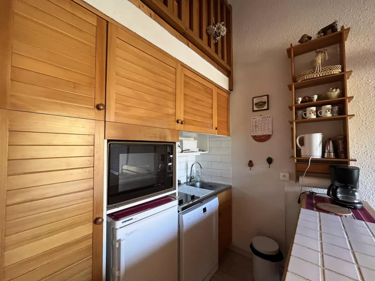 Kitchenette en bois équipée avec micro-ondes, lave-vaisselle, rangements en hauteur et étagères décorées dans un appartement de montagne.