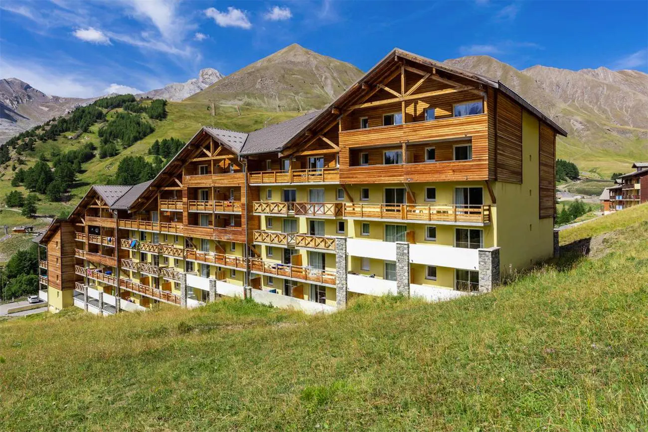 Façade en bois de la résidence Les Cimes du Val d’Allos, nichée au cœur des montagnes verdoyantes avec vue sur les pistes et sentiers alpins.