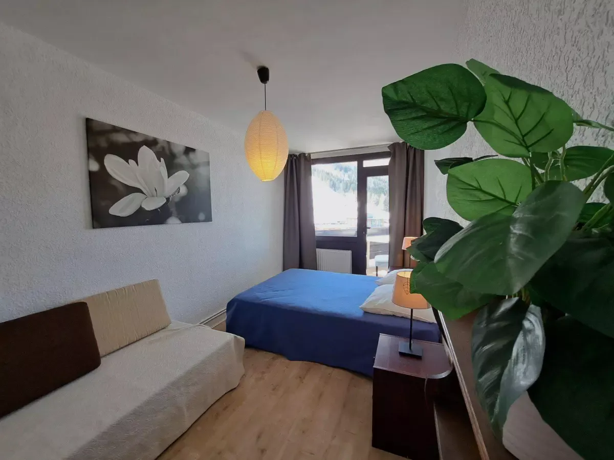 Chambre lumineuse avec lit double, canapé, décoration épurée et vue dégagée sur la montagne depuis une grande fenêtre.
