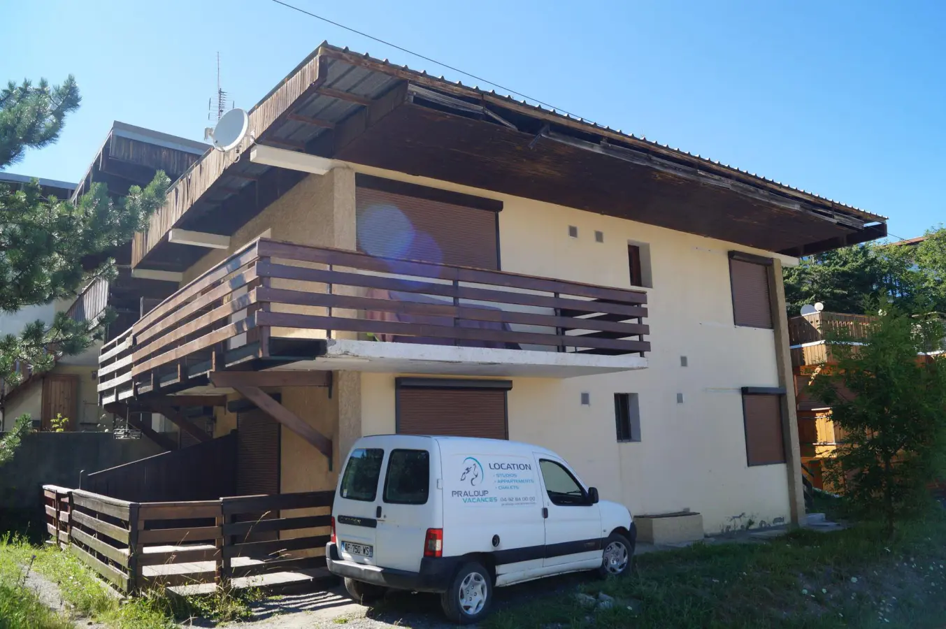 Façade extérieure de la résidence Pas du Loup avec balcons en bois, véhicule de location stationné et environnement calme en montagne.