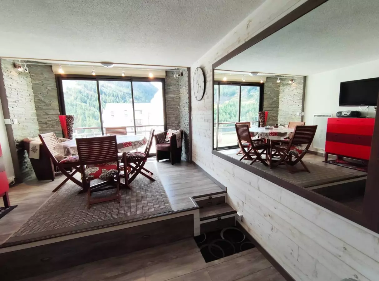 Séjour lumineux avec coin repas surélevé, grandes baies vitrées et vue dégagée sur la montagne.