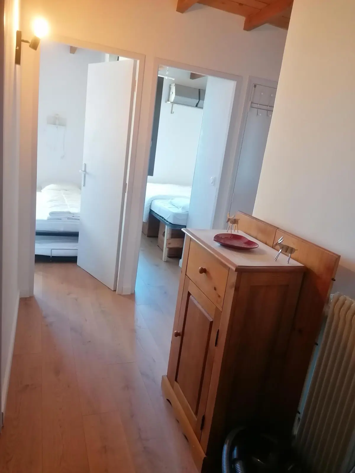 Couloir en parquet avec meuble en bois menant à deux chambres lumineuses dans un appartement de montagne confortable.
